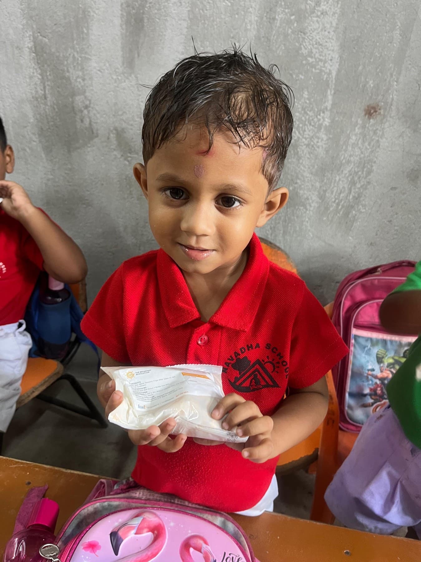 A young boy in a red school polo holds his packet of the nutrition mix.