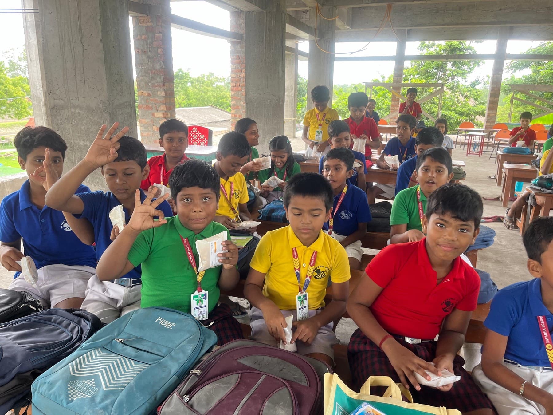 Two schoolgirls in uniform grin as they hold up small pieces of the puffed breakfast snack and a Breakfast Revolution packet at an open-air classroom.